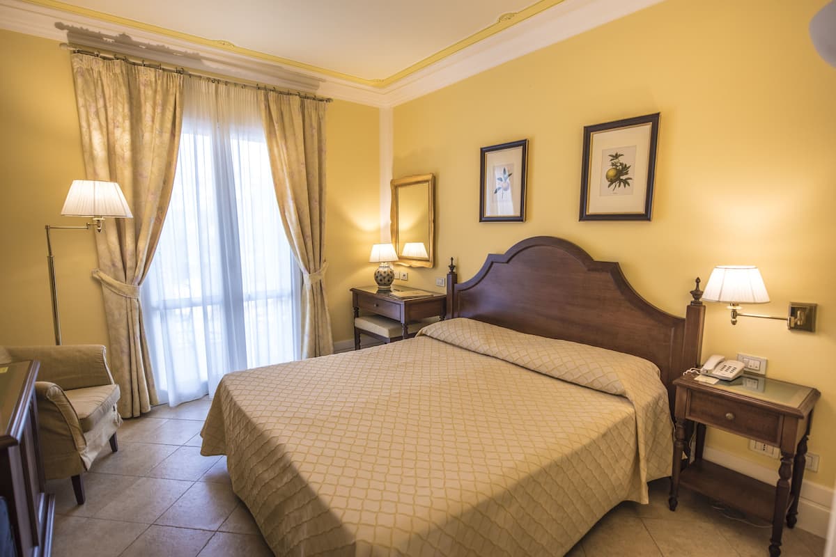 Ein Hotelzimmer mit einem großen Bett, einem Schreibtisch mit Lampe, einem Sessel und einem Nachttisch mit Telefon.