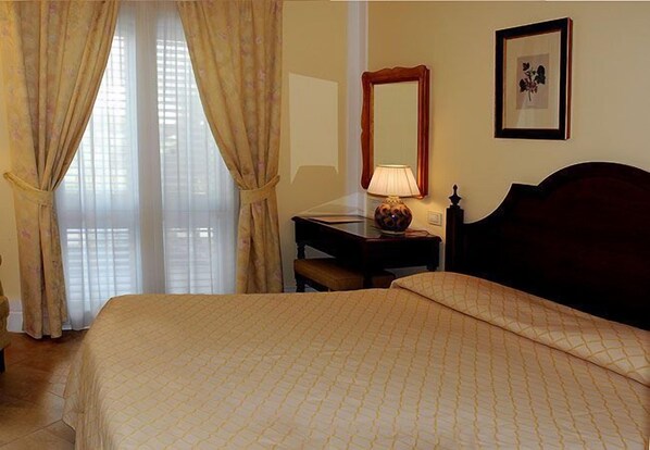 A hotel room with a bed, a desk, a lamp, a mirror, and a framed picture on the wall. - Hotel Villa Daphne (Giardini Naxos)