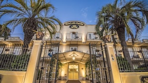 The entrance of Hotel Villa Daphne with a gated entrance, palm trees, and a sign above the door. - Hotel Villa Daphne (Giardini Naxos)