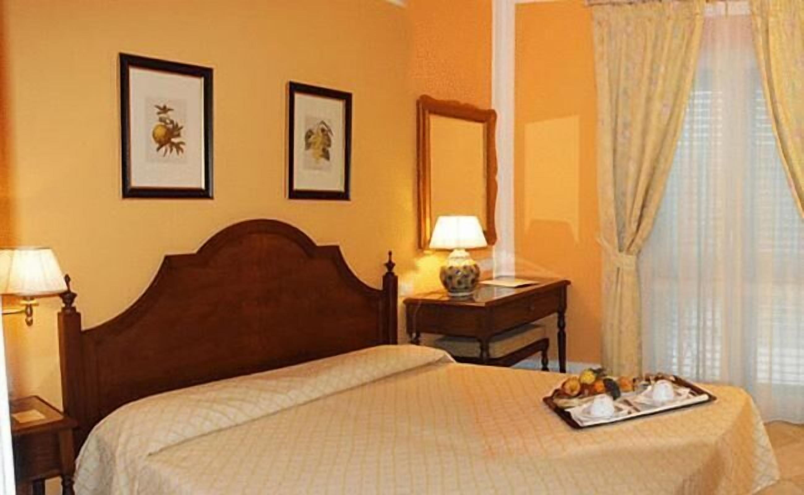 Una habitación de hotel con una cama, una mesita de noche con una lámpara, una pequeña mesa con lámpara y una bandeja con alimentos para el desayuno.