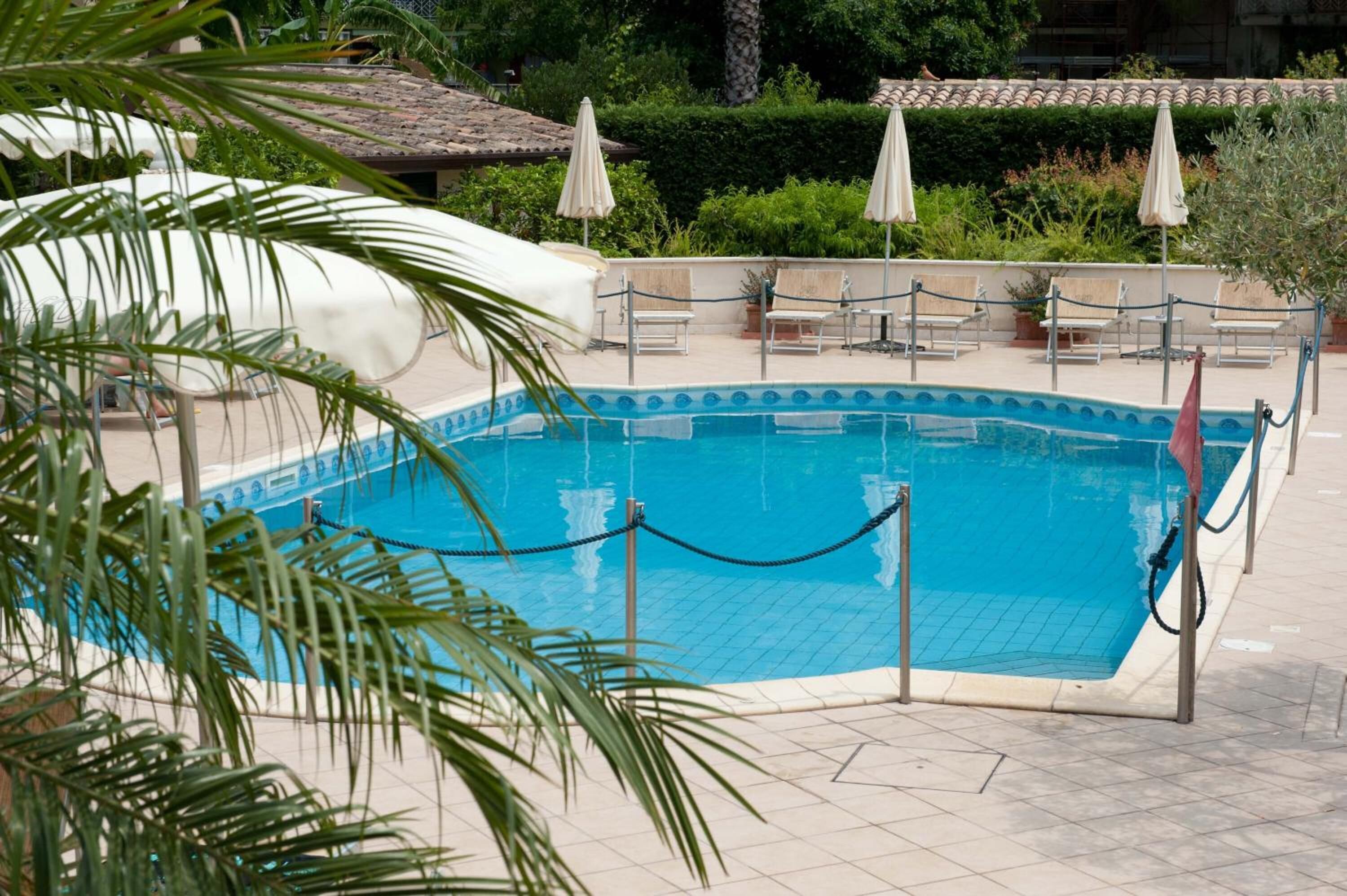 A pool area with a tiled deck, lounge chairs, and umbrellas.