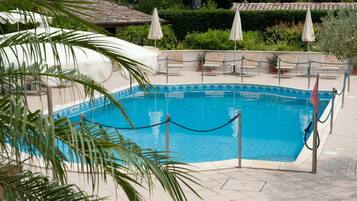 A pool area with a tiled deck, lounge chairs, and umbrellas.