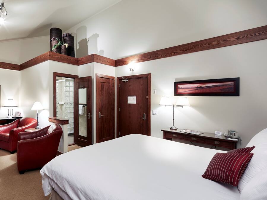 A hotel room with a large bed, a desk, a chair, a wardrobe, and a bathroom visible through an open door.