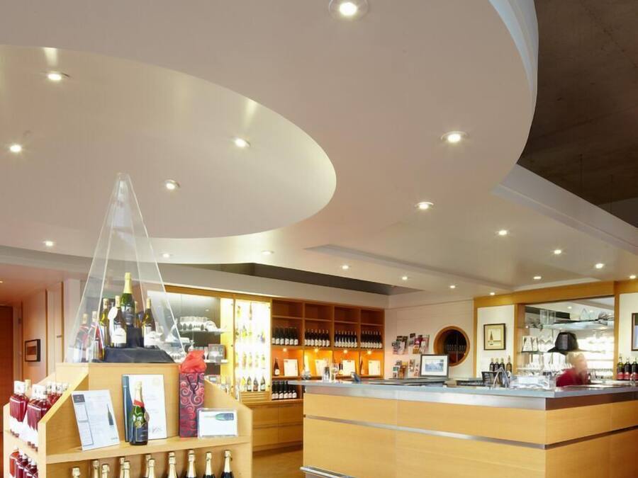A modern bar area with a curved ceiling, wooden shelves with bottles, and a counter.