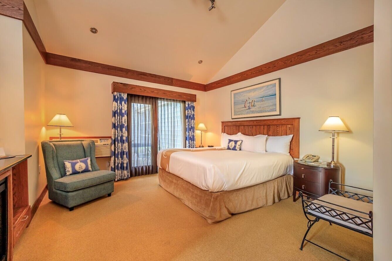 A hotel room with a bed, a chair, a desk, and a window with curtains.