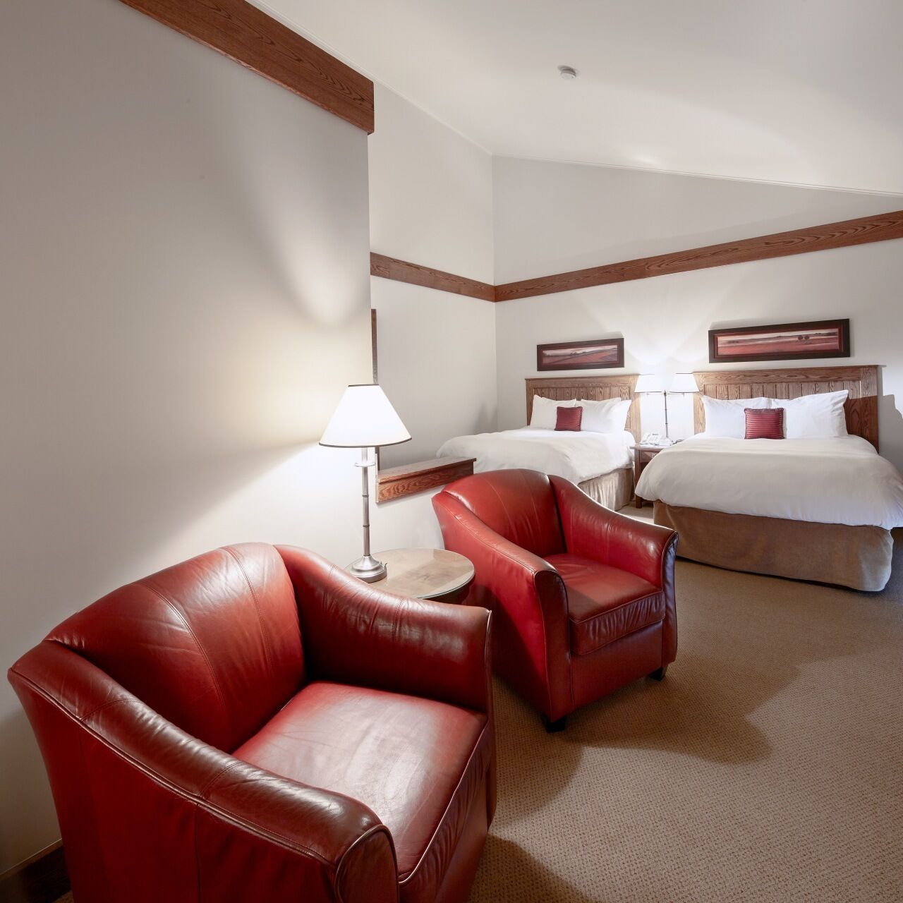Une chambre d’hôtel avec deux lits, un canapé en cuir rouge, une petite table avec une lampe et des poutres en bois au plafond.
