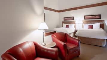 Una habitación de hotel con dos camas, un sofá de cuero rojo, una mesita con una lámpara y vigas de madera en el techo.