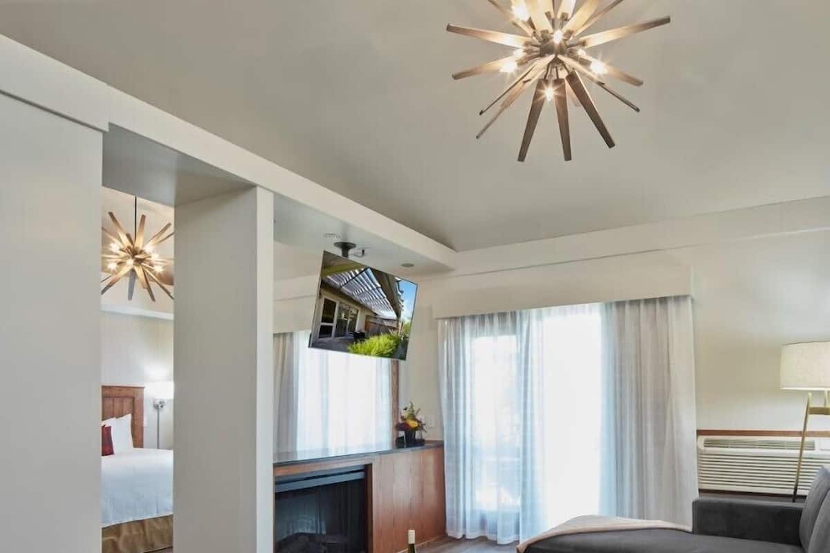 A modern hotel room with a round wooden coffee table, grey sofas, a fireplace, and a TV mounted on the wall.