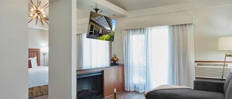 Een moderne hotelkamer met een ronde houten salontafel, grijze banken, een open haard en een aan de muur bevestigde televisie.