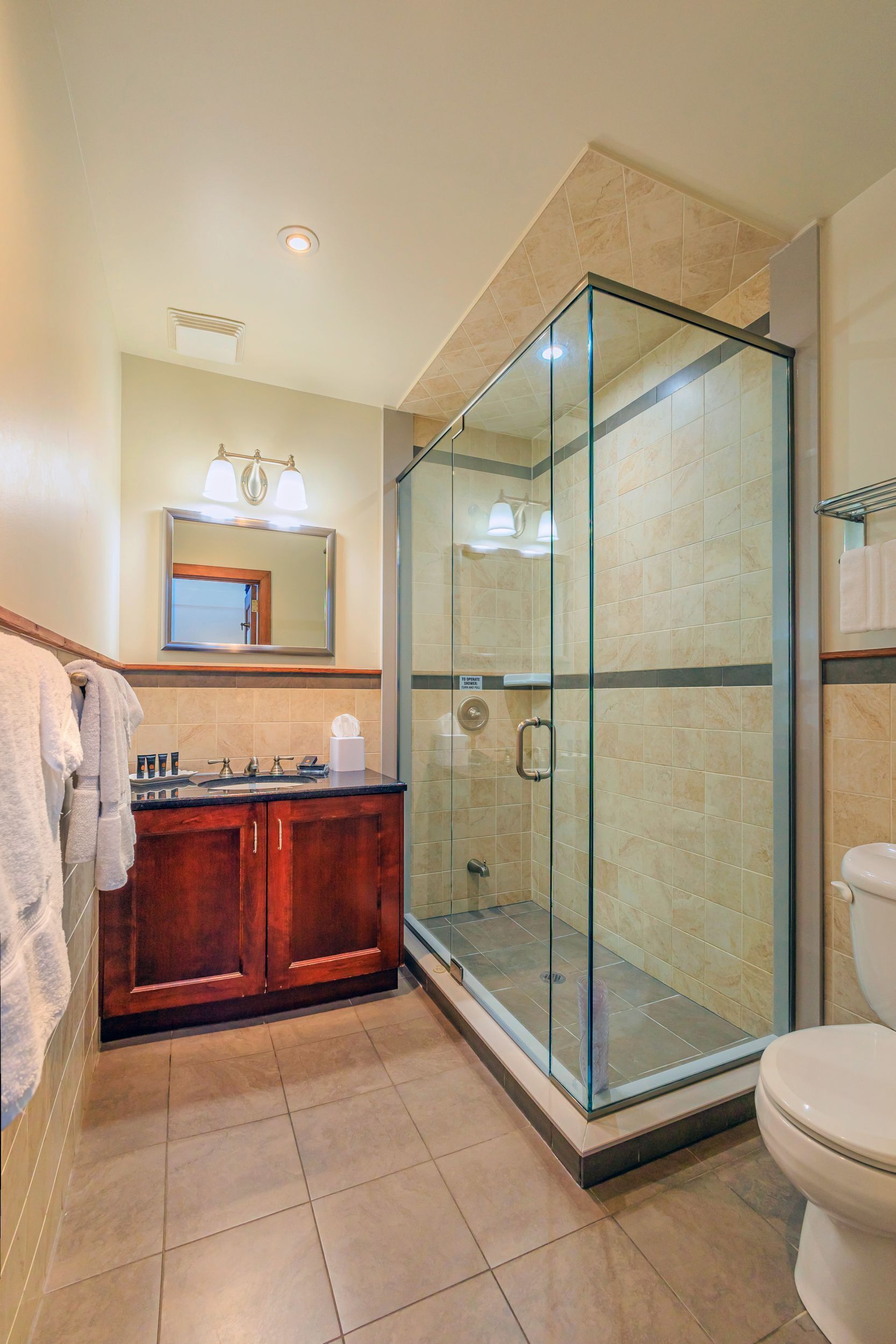 Un baño moderno con ducha de vidrio, tocador de madera, lavamanos y retrete.