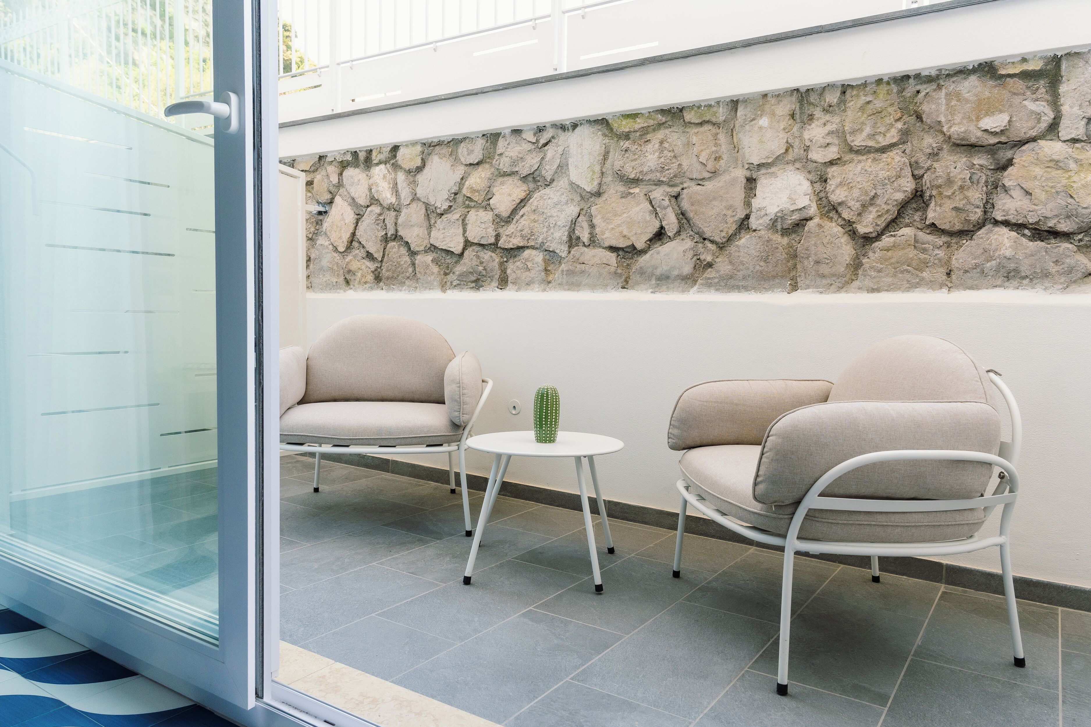 A modern outdoor seating area with two cushioned chairs, a small round table, and a cactus decoration.