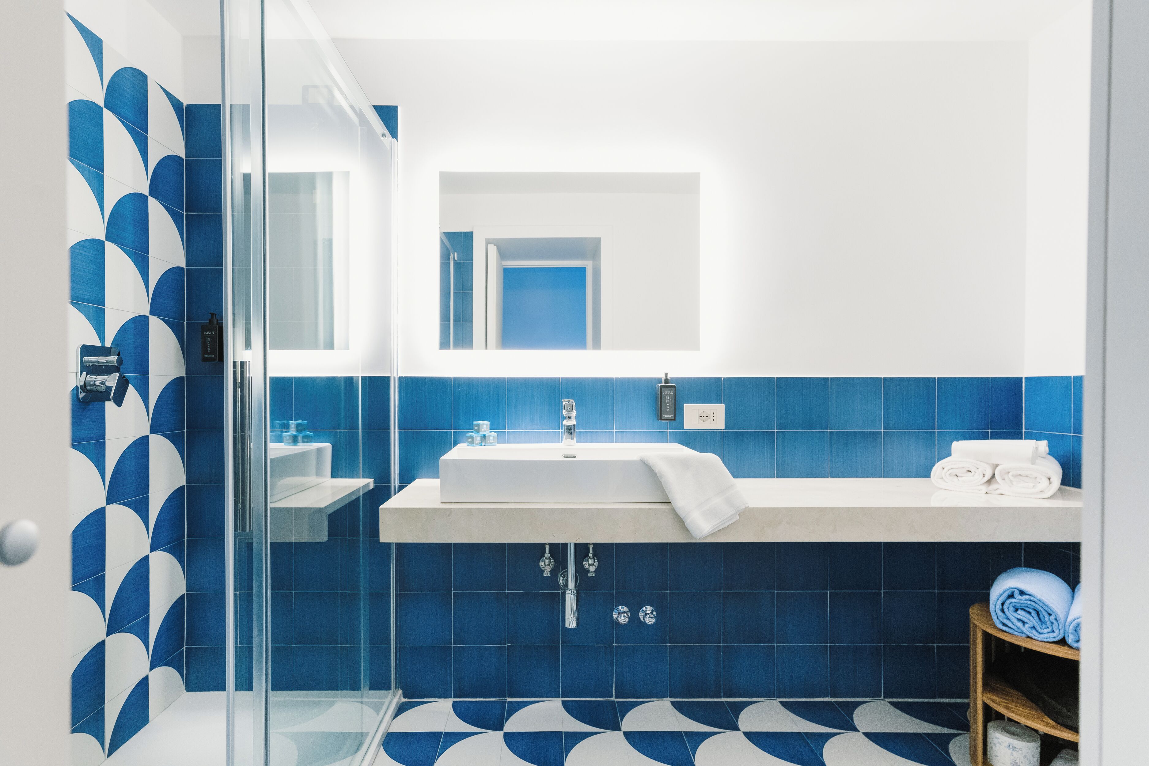 Un baño moderno con cabina de ducha de vidrio, un lavabo blanco y paredes con azulejos azules.