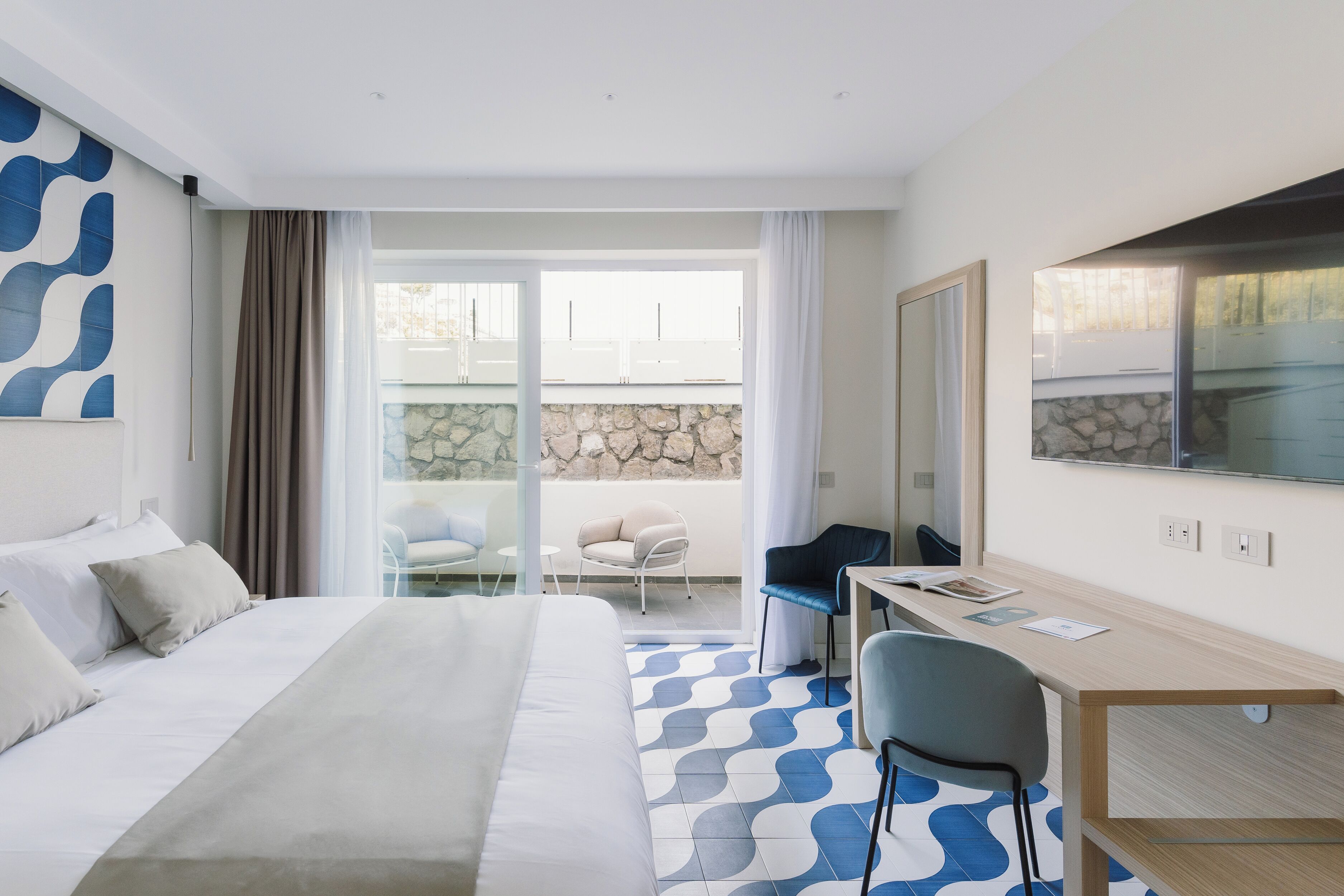 Habitación de hotel con cama, escritorio, silla y un amplio ventanal con vistas al exterior.