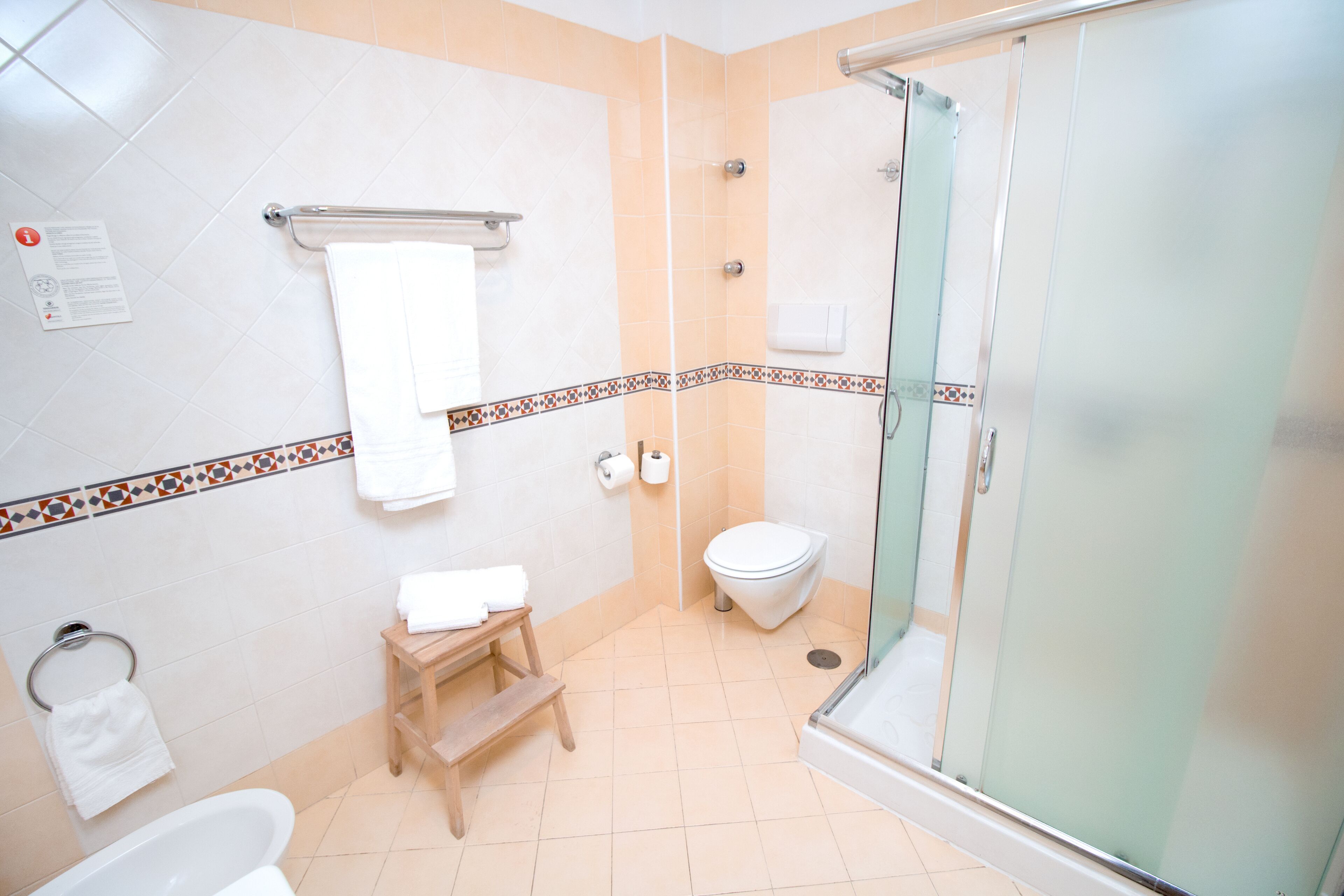 Une salle de bain avec une douche à parois de verre, des toilettes, un lavabo et un petit tabouret en bois.