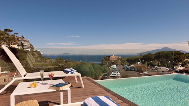 A poolside area with lounge chairs, a table with drinks, and a view of a coastal landscape.