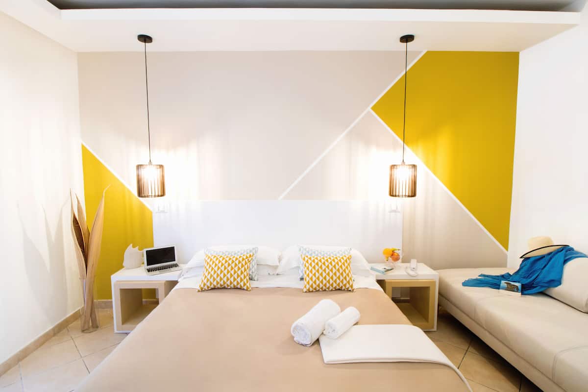 A modern hotel room with a large bed, two bedside tables, a sofa, and a desk with a laptop.