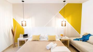A modern hotel room with a large bed, two bedside tables, a sofa, and a desk with a laptop.
