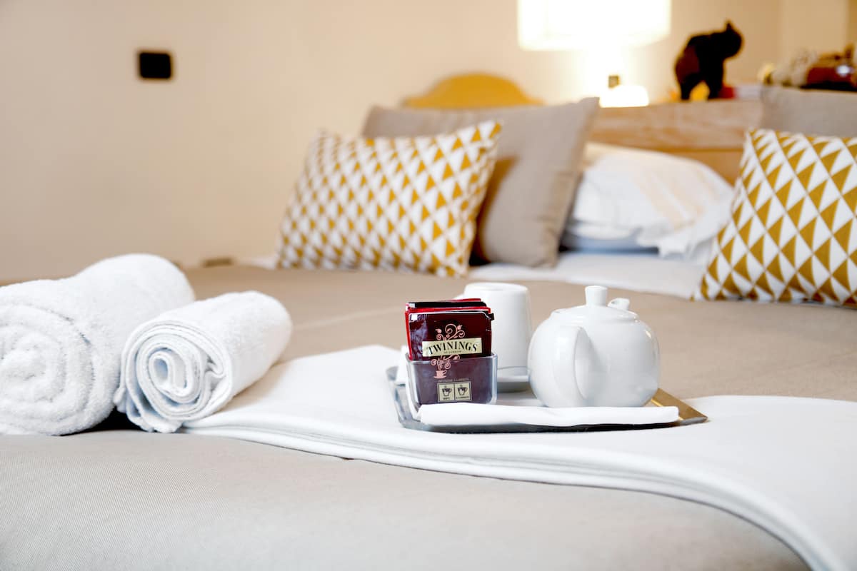 A neatly made bed with rolled white towels, a tea set, and a small box of Twinings tea on a tray.