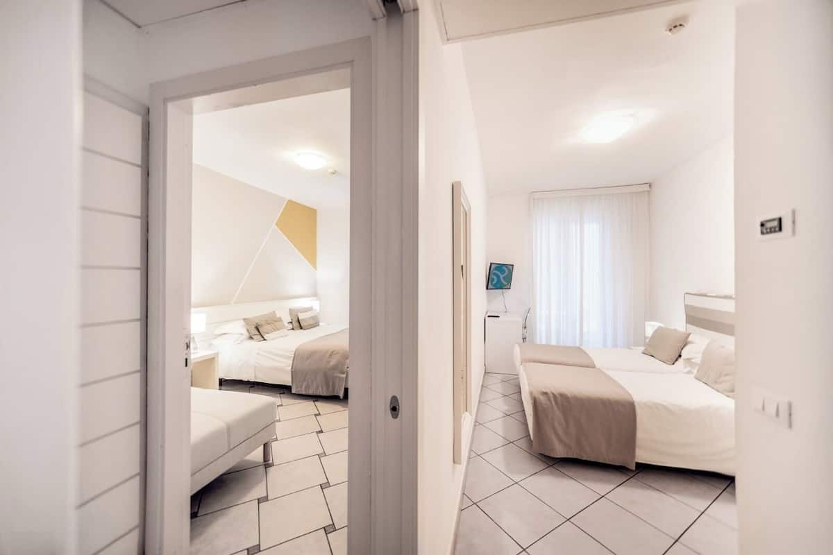 A modern hotel room with two beds, a desk, and a large window with curtains.