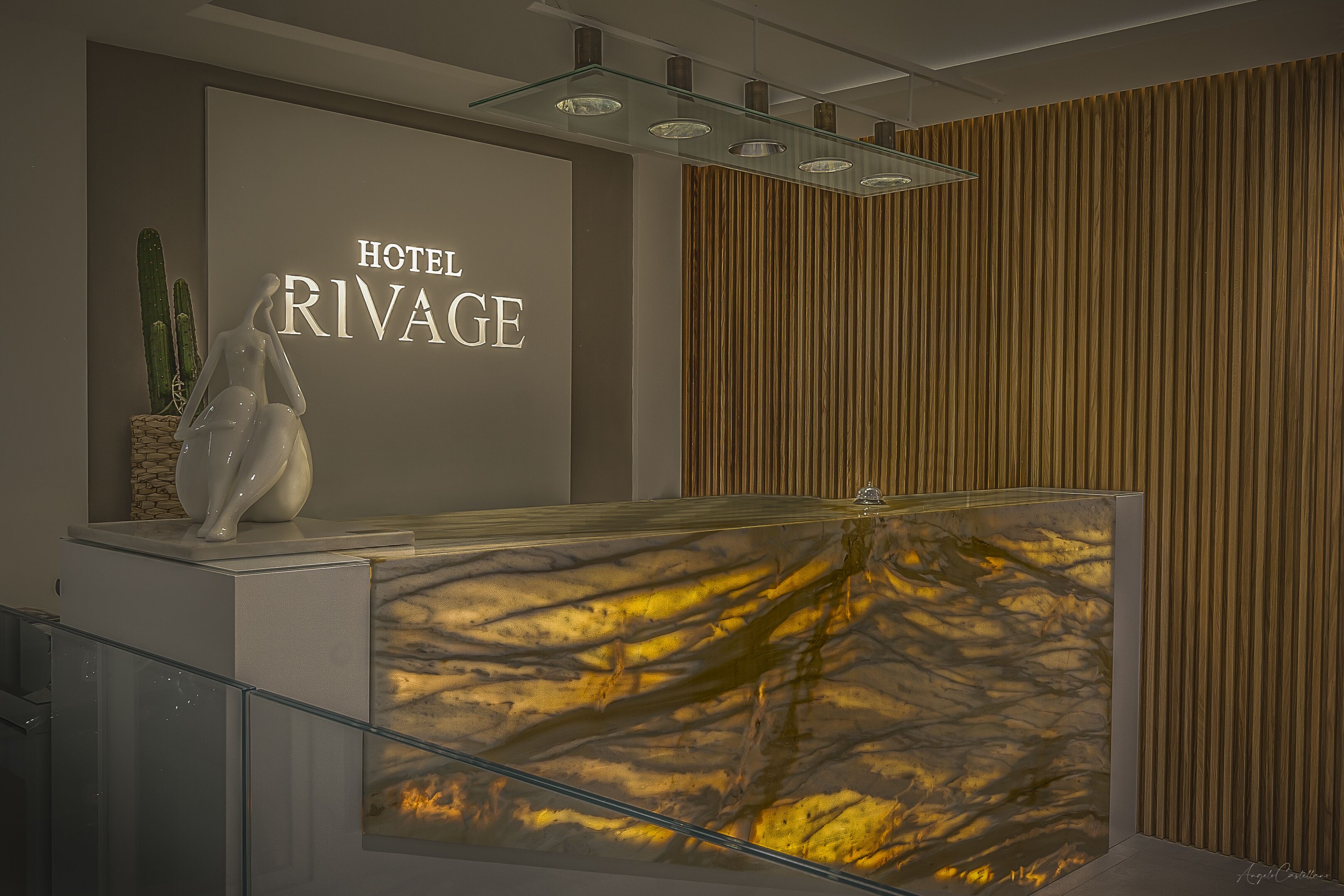 Un área de recepción de diseño moderno, con una mesa de recepción, un letrero mural que dice “HOTEL RIVAGE” y una planta de cactus decorativa.