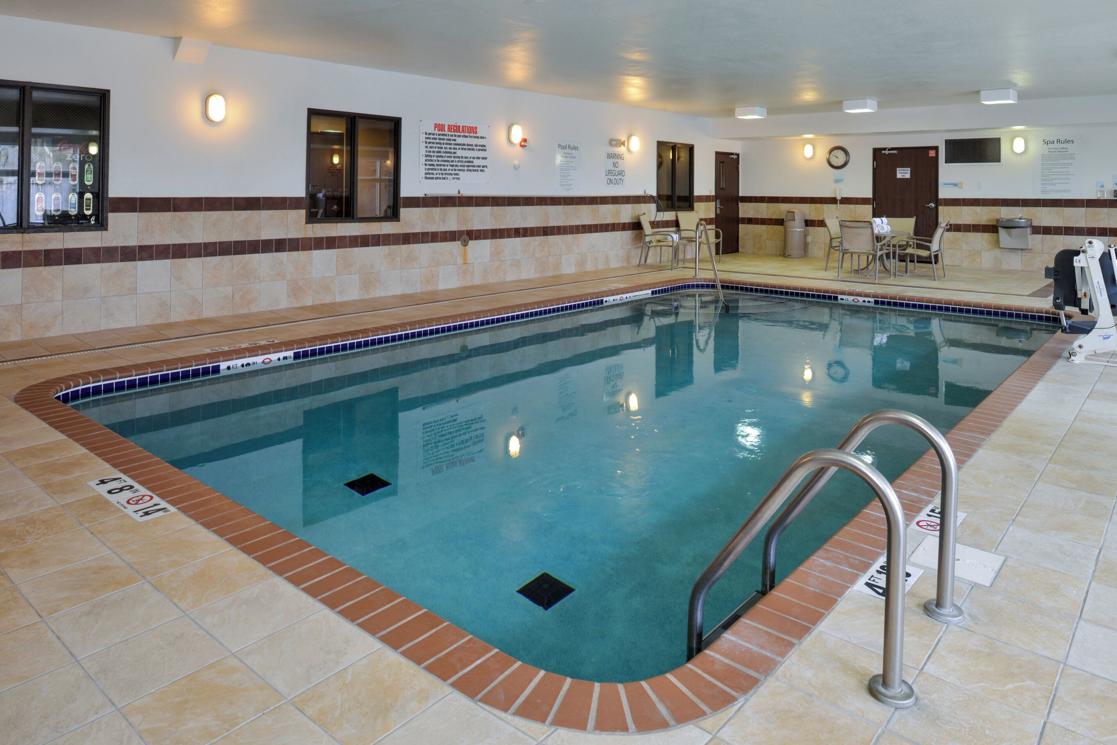A swimming pool with clear water, tiled edges, and a lifeguard warning sign.
