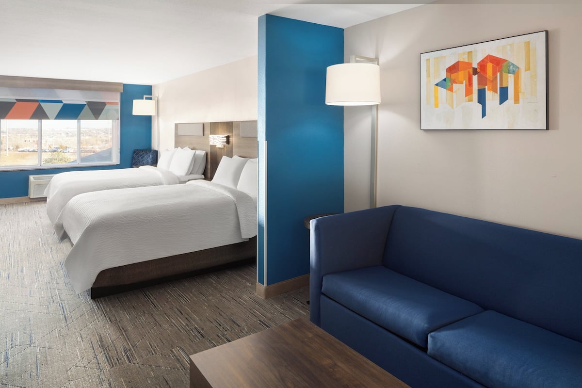 A hotel room with two beds, a blue sofa, a wooden coffee table, and a city view.