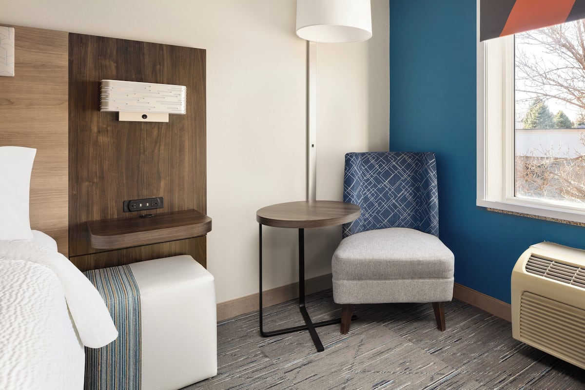 A hotel room with a bed, a small table, a chair, a heater, and a window with a view.