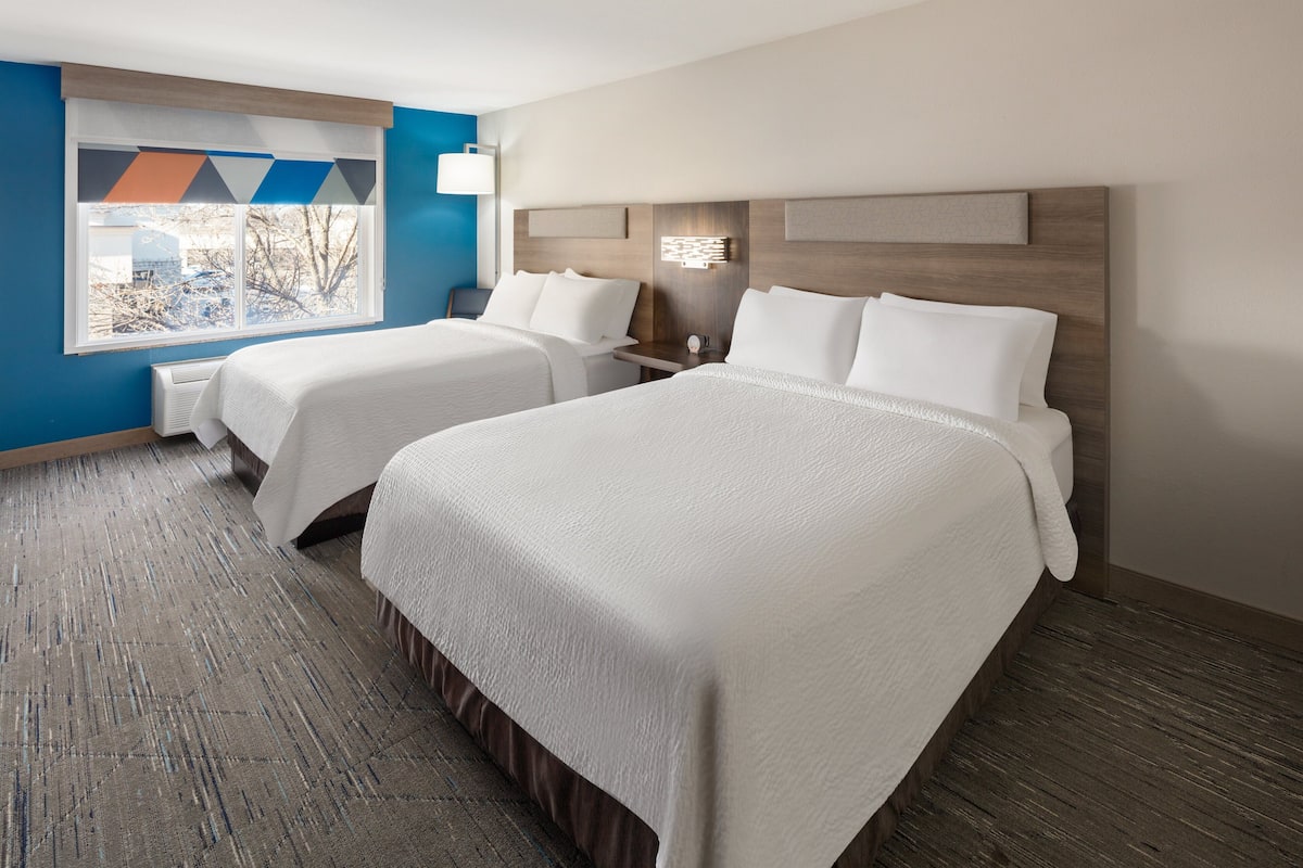 A hotel room with two beds, a large window with a view, and a modern design.