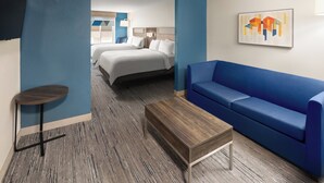 Habitación de hotel con sofá azul, una mesita de centro de madera, una mesa redonda pequeña y dos camas.