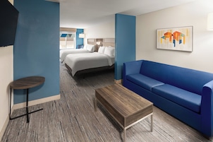 Habitación de hotel con sofá azul, una mesita de centro de madera, una mesa redonda pequeña y dos camas.