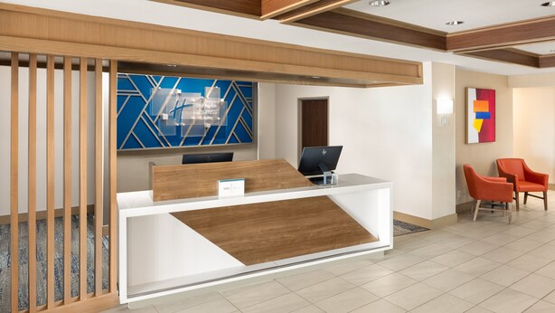 A reception area with a wooden reception desk, two orange chairs, and a blue geometric wall art piece.