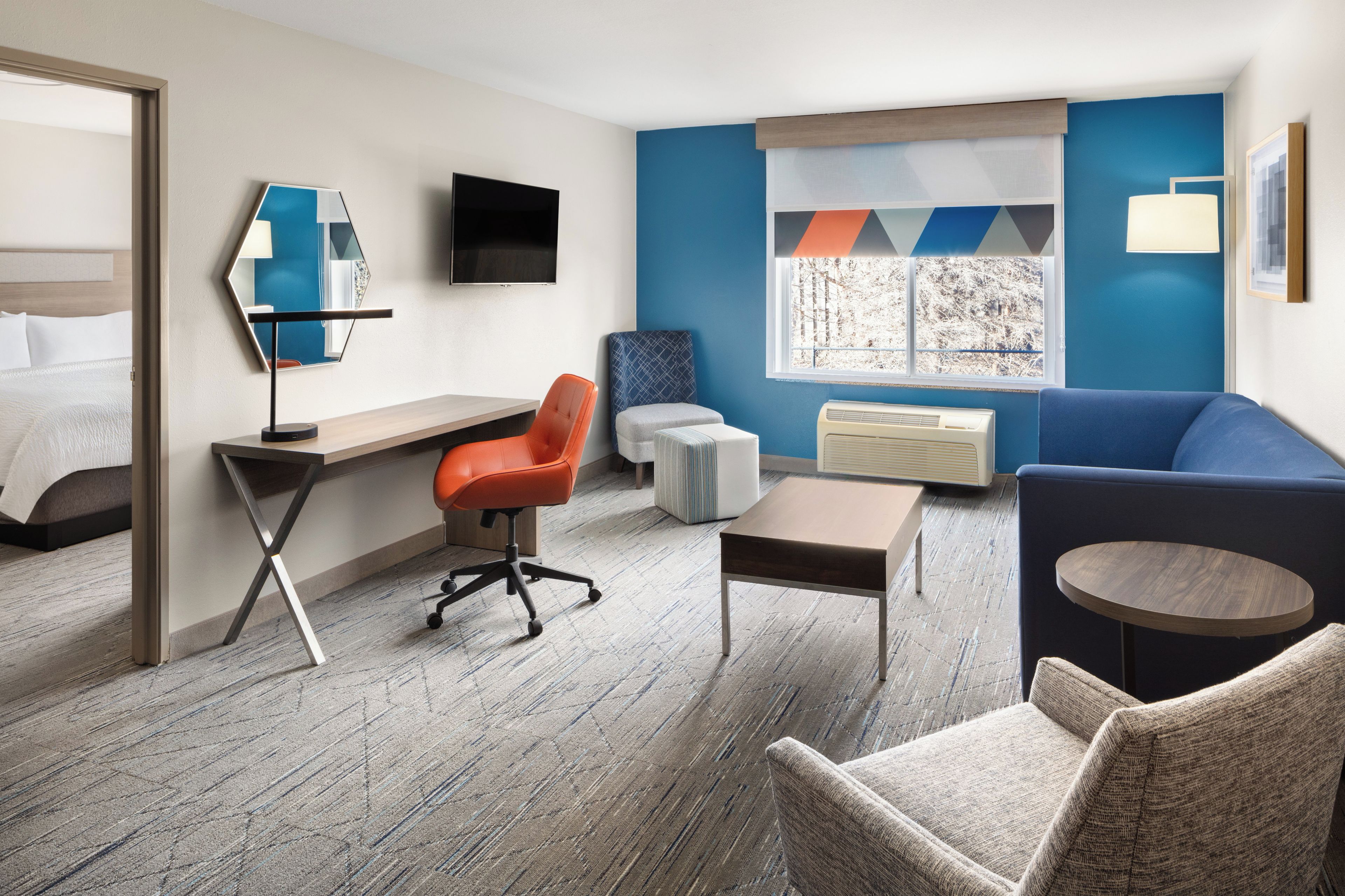 Une chambre d’hôtel équipée d’un lit, d’un bureau, d’une chaise, d’un canapé, d’une télévision, d’une fenêtre avec vue et d’un climatiseur fixé au mur.