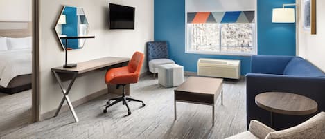 A hotel room with a bed, a desk, a chair, a sofa, a TV, a window with a view, and a wall-mounted air conditioner.