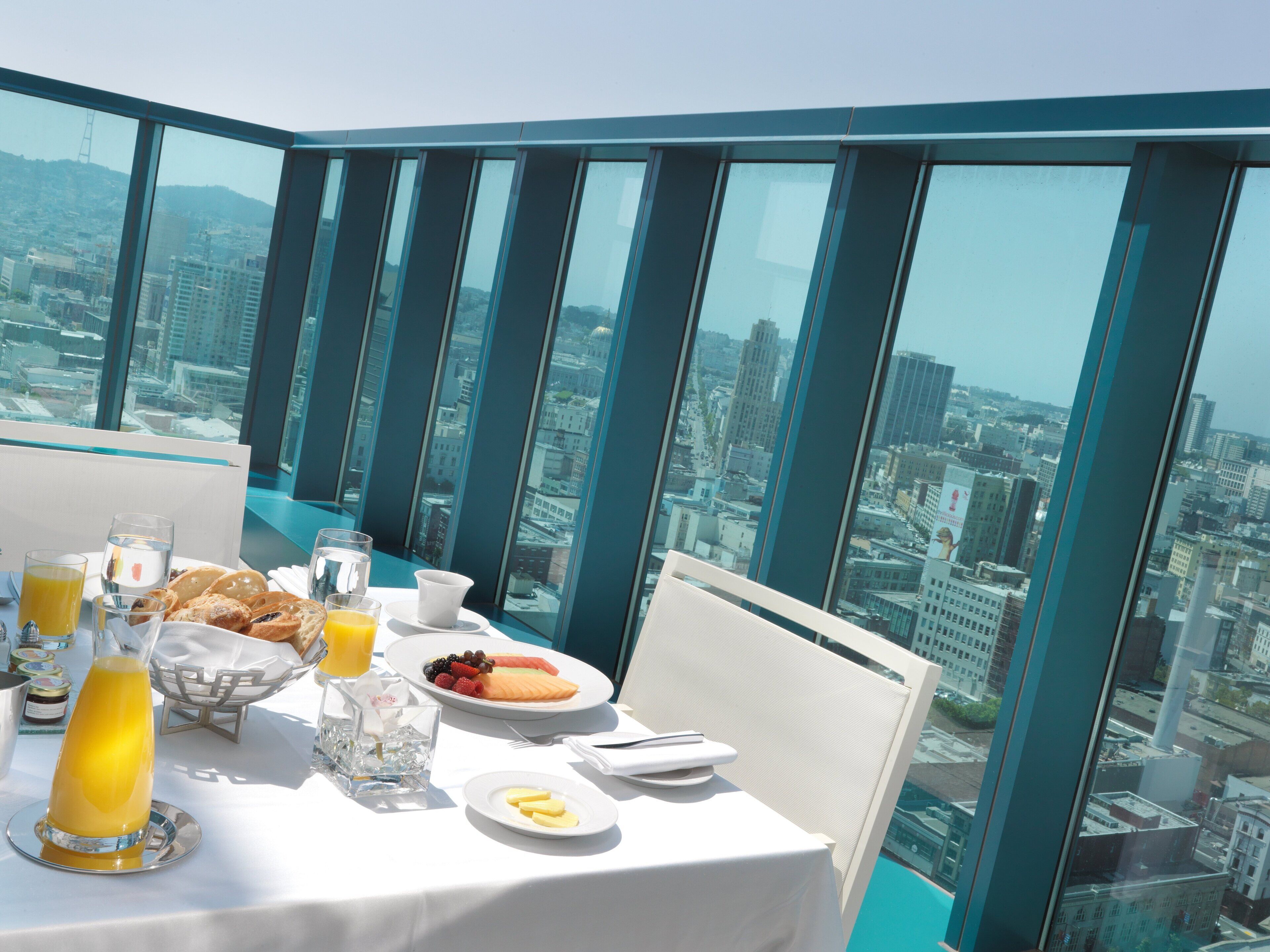 Un comedor en un edificio alto con vistas a la ciudad, una mesa dispuesta para el desayuno y un separador de vidrio.