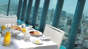 Un comedor en un edificio alto con vistas a la ciudad, una mesa dispuesta para el desayuno y un separador de vidrio.