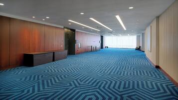 A spacious hotel lobby with a patterned carpet, wooden paneling, and a long corridor leading to a conference room.