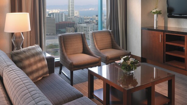 A hotel room with a large window, a sofa, two armchairs, a coffee table, a lamp, and a TV. - InterContinental San Francisco by IHG (San Francisco)