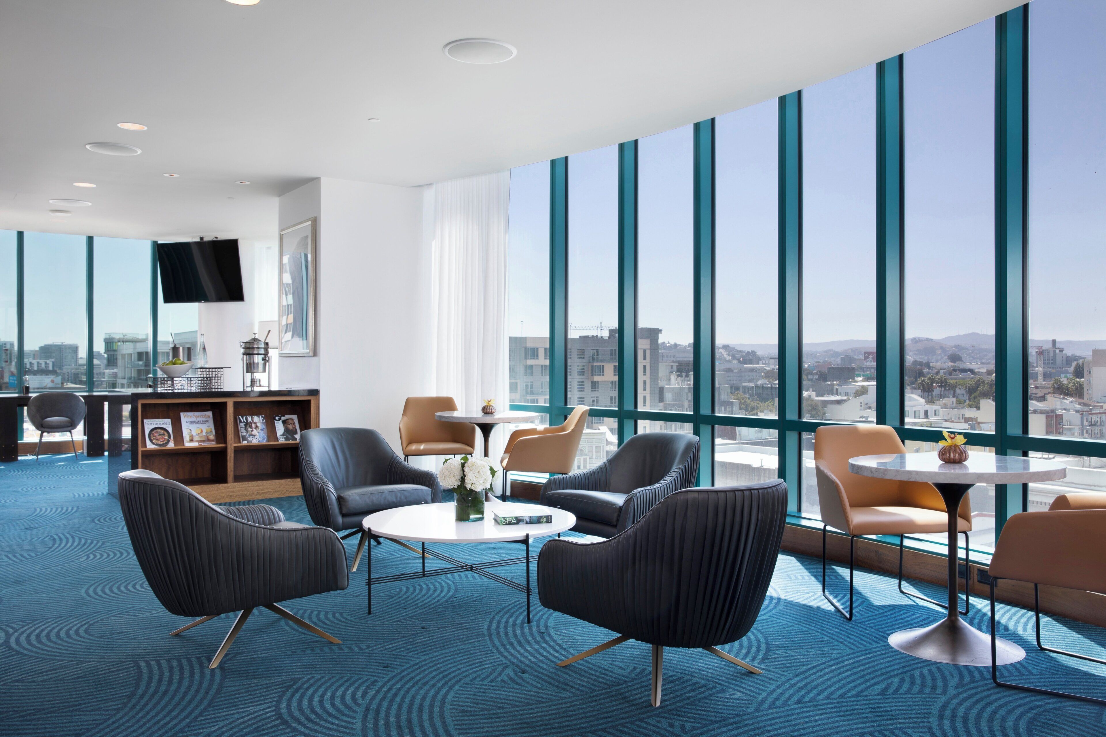 Eine moderne Hotelhalle mit großen Fenstern, bequemen Sitzgelegenheiten, einem kleinen Tisch und einem Bücherregal.