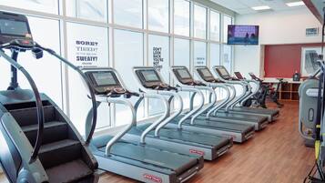 A gym with multiple treadmills lined up against a wall with motivational posters.