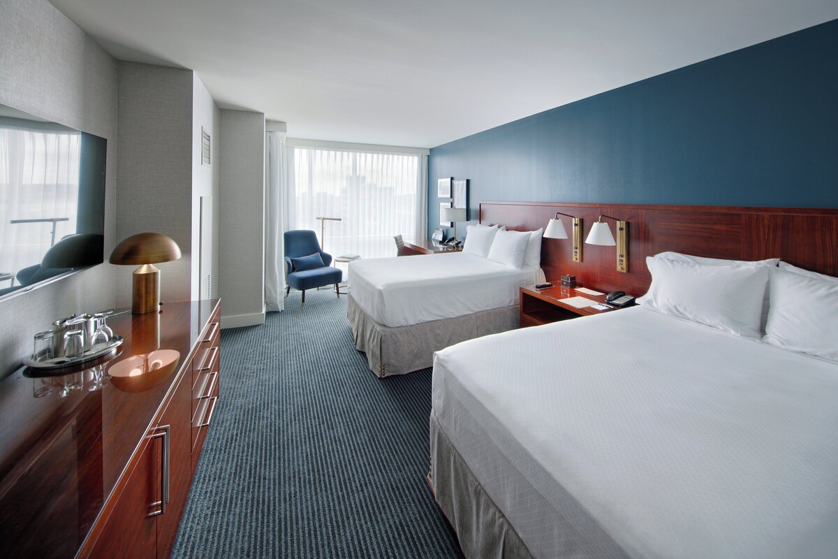 Une chambre d’hôtel avec deux lits, un bureau avec une lampe, une chaise et un téléviseur.