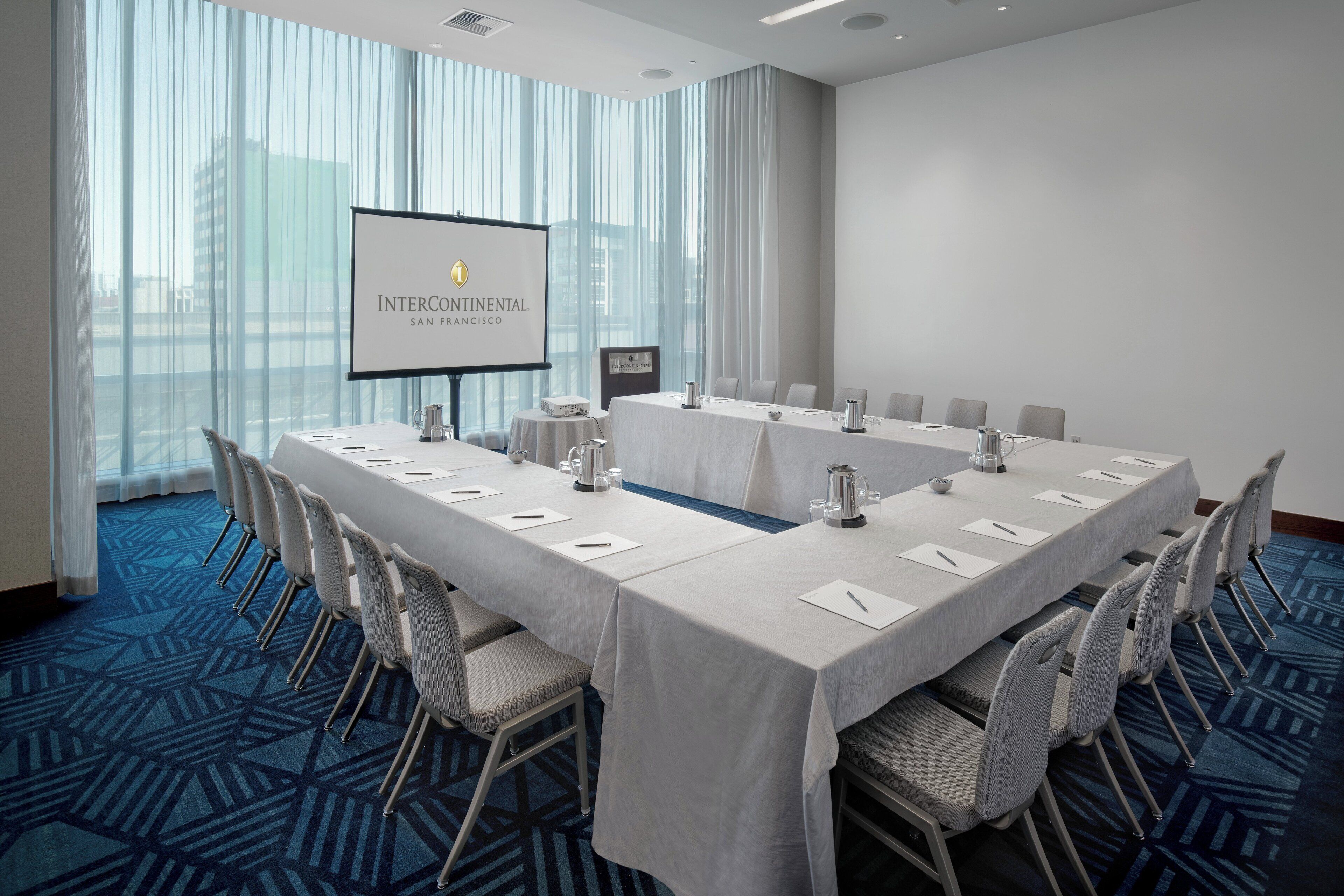 A conference room with a long table, chairs, a projector screen, and a city view.