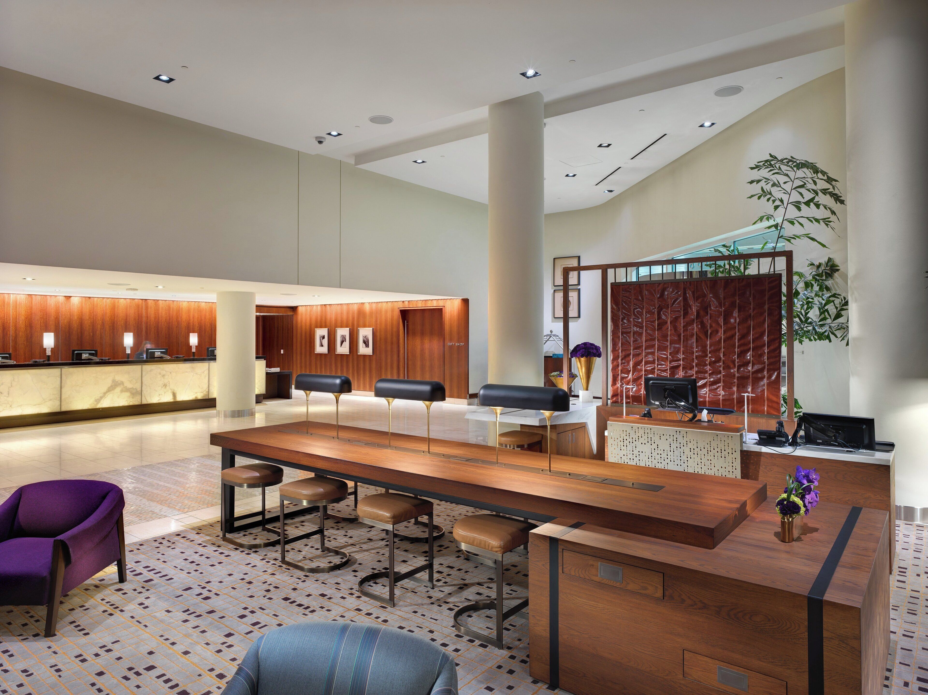 A modern hotel lobby with a reception desk, seating area, and a large plant.