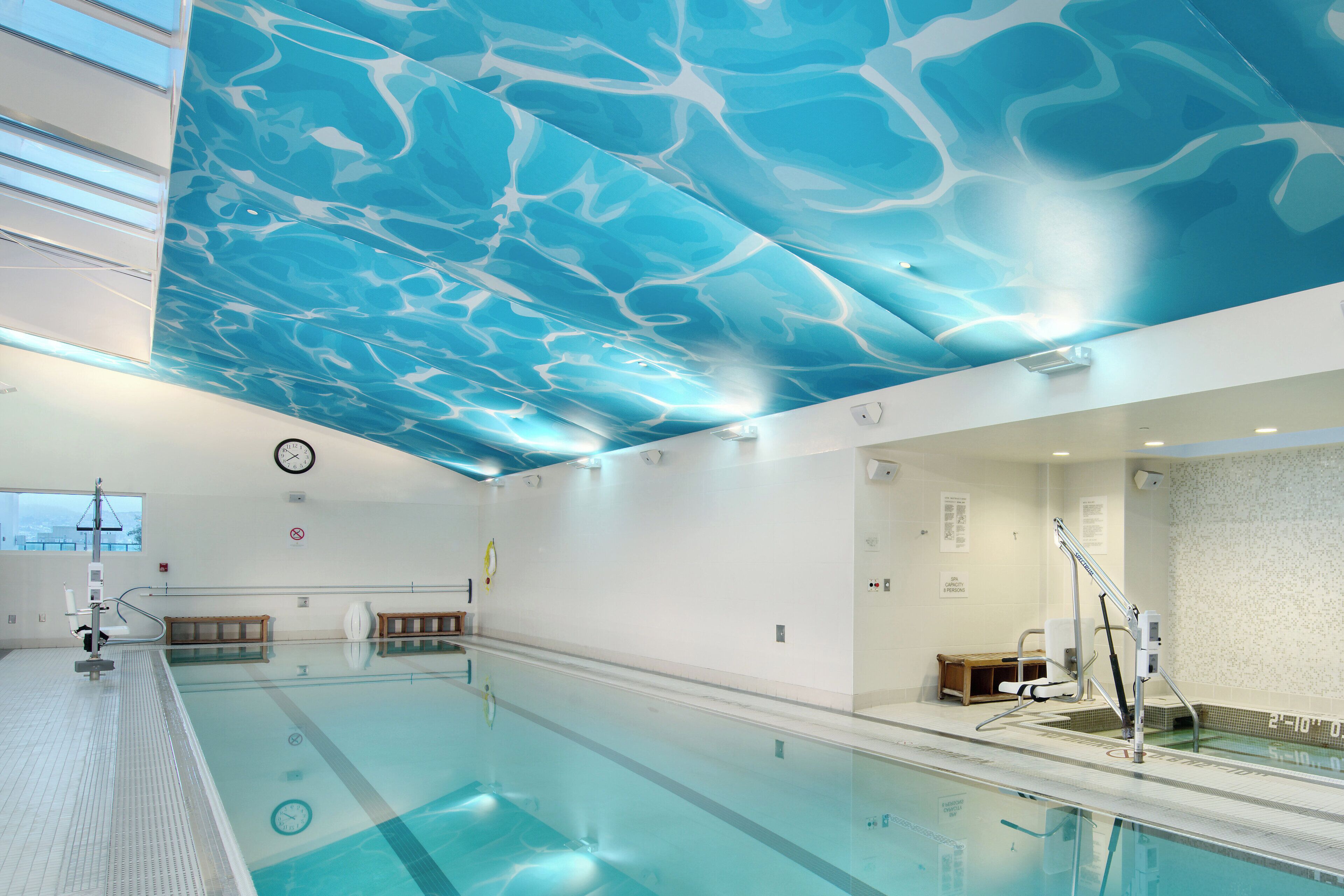 Une piscine dont le plafond présente un motif ondulé, avec une horloge et un panneau indiquant la capacité maximale de personnes autorisées dans le spa.