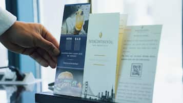A hand holding a brochure with a burger and a bar sign, and another brochure with a QR code and text.