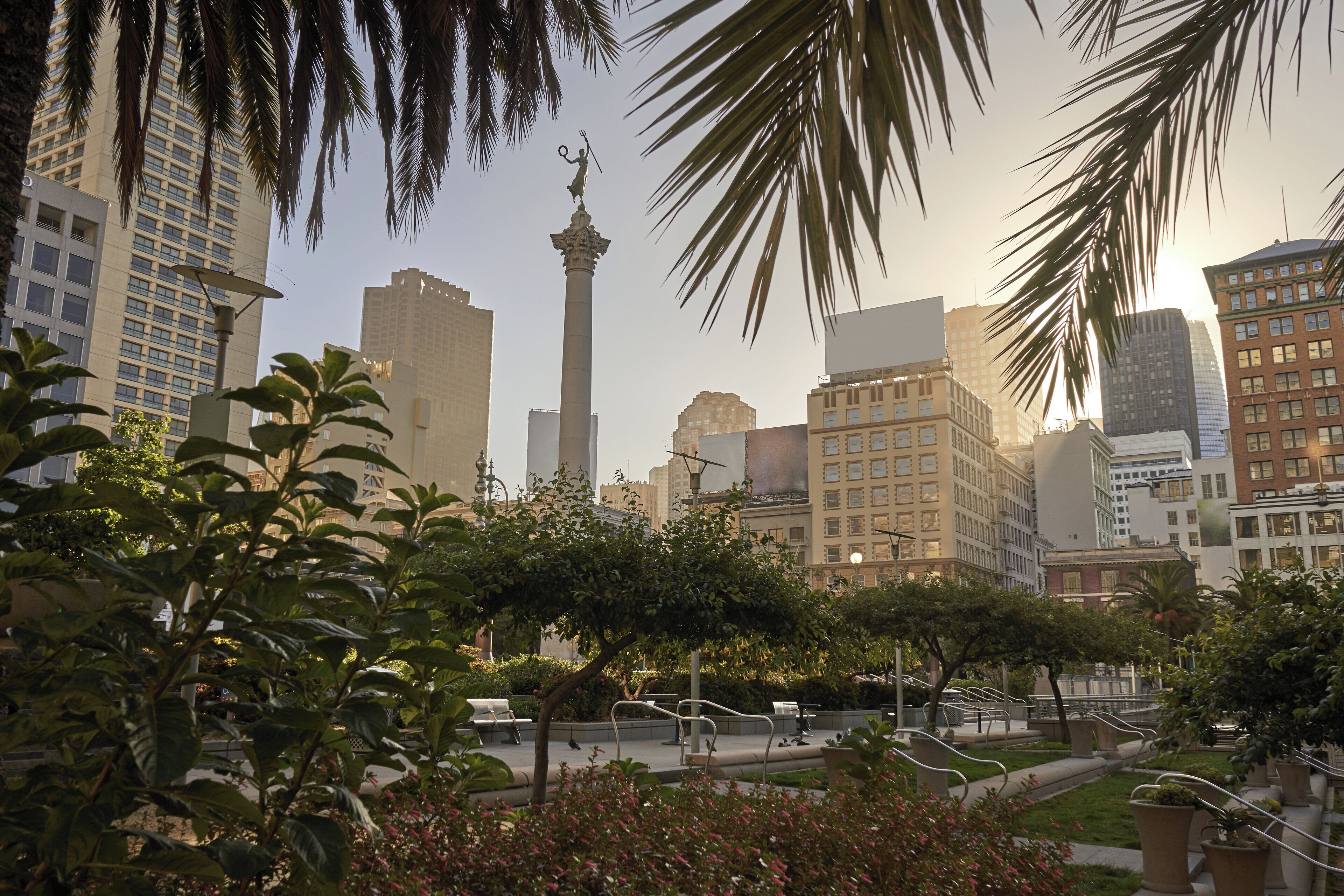 Un paisaje urbano con edificios altos, un monumento destacado y un parque con bancos y senderos.