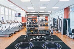 Une salle de sport équipée de tapis de course, d’appareils de musculation et d’un téléviseur fixé au mur.
