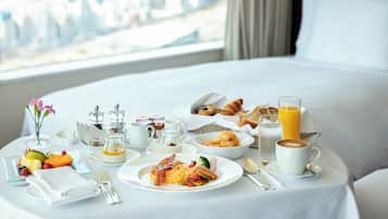 A breakfast setup on a bed with a city view, including plates of food, a glass of orange juice, and a cup of coffee.