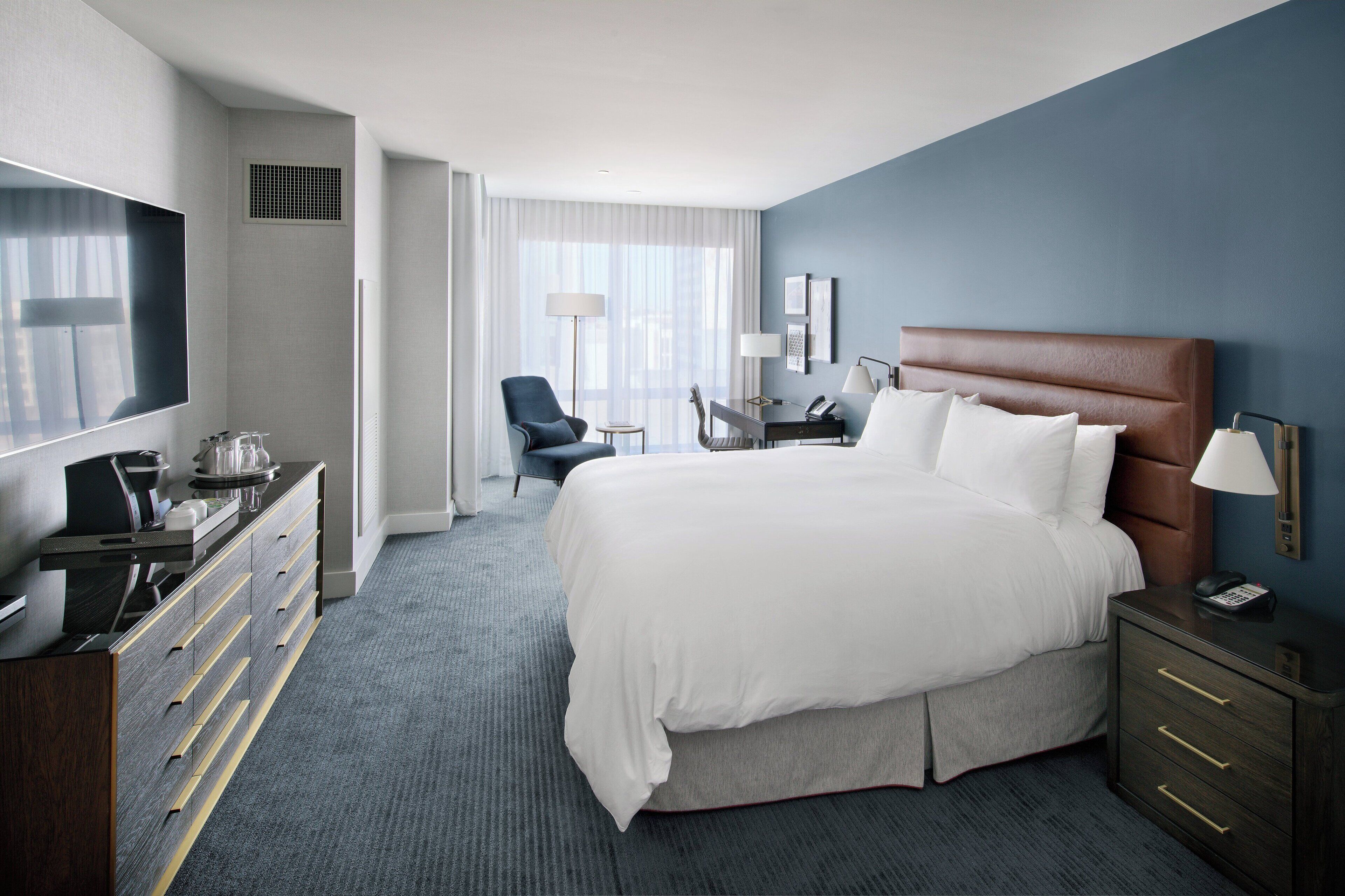 Ein Hotelzimmer mit einem großen Bett, einem Schreibtisch, einem Sessel, einem Fernseher und einer Kommode.