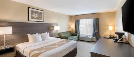 A hotel room with a large bed, a desk, a chair, a television, and a window with curtains.
