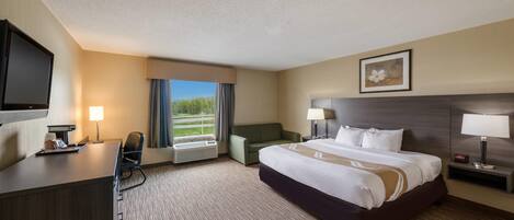 A hotel room with a large bed, a desk with a computer, a TV, and a window with curtains.